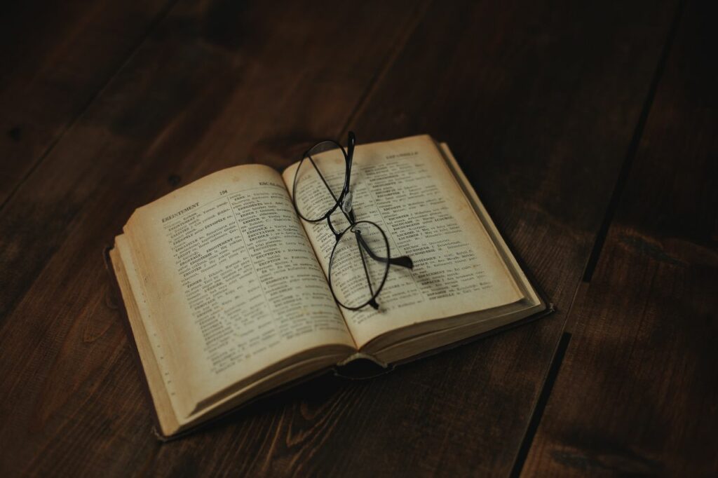 Open vintage book with eyeglasses resting on a wooden surface, evoking a sense of nostalgia.